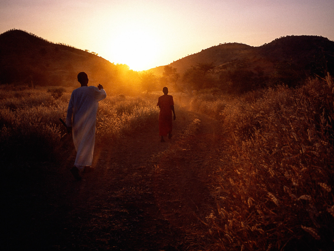 two people walk into the sunset away from camera (Nuba Mountains, Sudan)